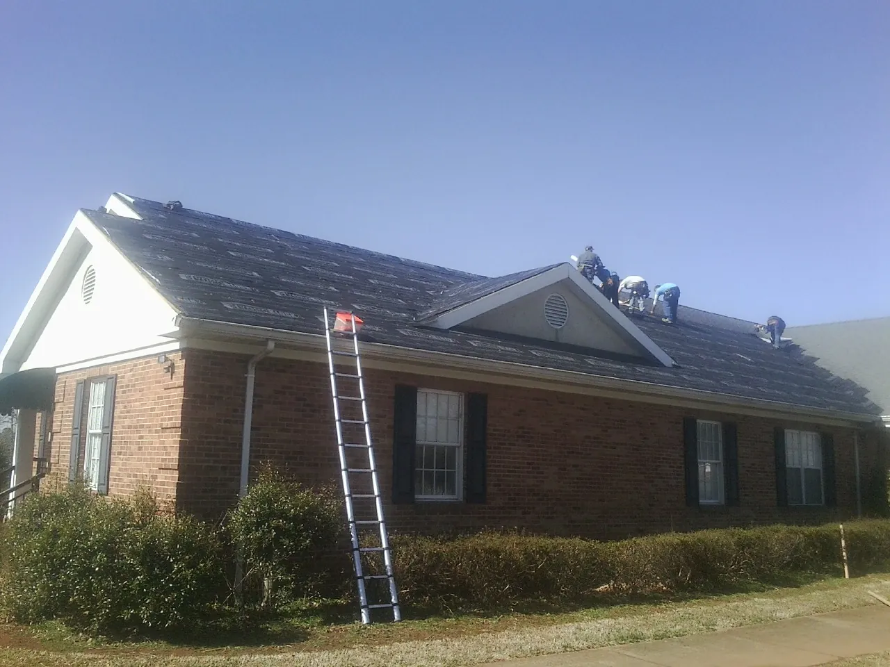 Crew tearing shingles off a brick ranch roof with a ladder set — Emergency Roof Repair work by our crew in Salyer