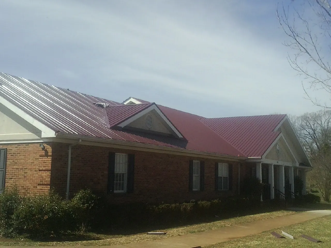 Red metal roof with gabled entries on a long brick building, from a Hail Damage Roof Repair job in Salyer